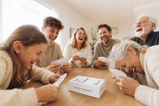 Familie spielt Cards For Christianity am Tisch und lacht