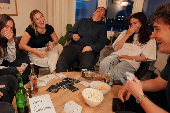 Junge Erwachsene lachen beim Spielen von Cards For Christianity am Tisch